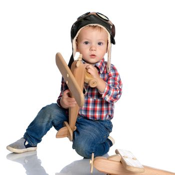 The boy in the helmet of the pilot plays with a toy wooden plane. He dreams of becoming a pilot. Concept of happy childhood, child in the family.Isolated on white background.