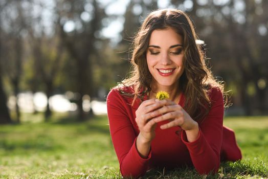 Portrait of young woman rest in the park smiling with a dandelion in her hair, lying on the grass