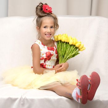 Happy little girl with a bouquet of flowers sitting on the couch. The concept of a holiday, a spring mood.