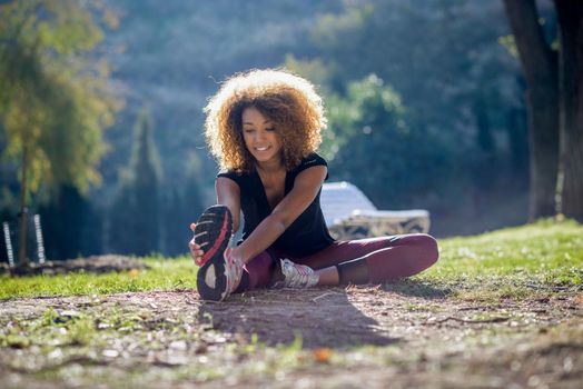 young fitness black woman runner stretching legs after run