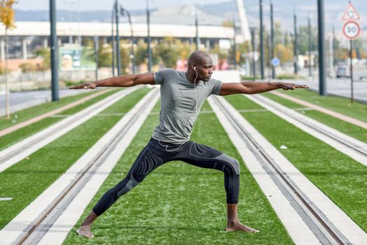 Black man practicing yoga in urban background. African male doing workout outdoors.