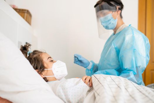 Doctor protected by personal protective equipment examining a little girl with a stethoscope at home.