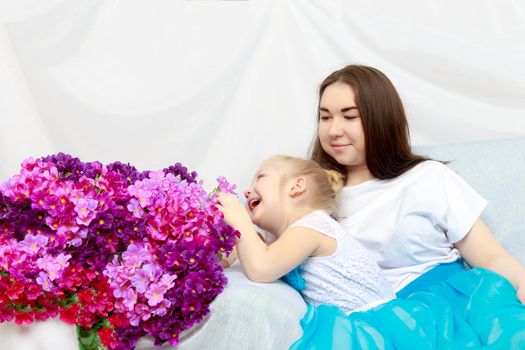 Sisters grow old and younger hugs on the couch.With a bouquet of flowers.