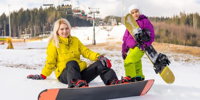 Mother and daughter with snowboards are playing in the snow