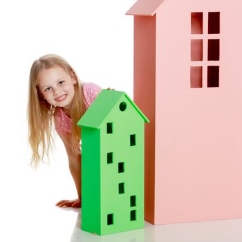 A cute little girl is playing with wooden houses. The concept of family happiness, play, creative development of the child.