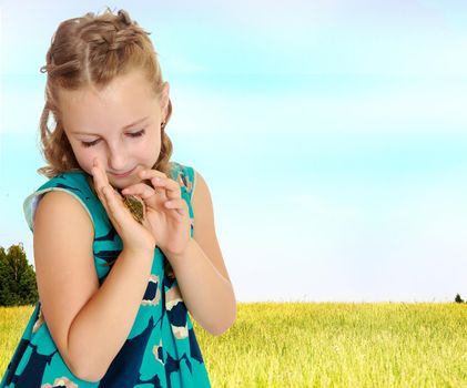 Attentive little girl looking at in the palms of a small turtle. Closeup.On the background of green grass and blue sky with clouds.