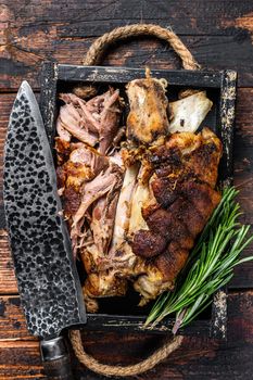 Roasted pork knuckle eisbein meat in a wooden tray with knife. Dark wooden background. Top view.