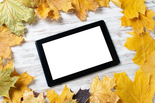 Tablet computer with blank screen lies on vintage wooden desk with bright foliage. Flat lay composition with autumn leaves on white wooden surface. Internet communication and digital technology