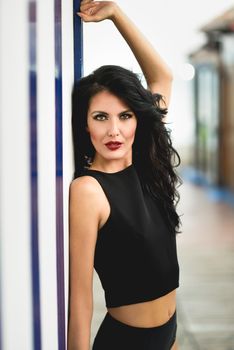 Young woman, model of fashion, wearing black top and panties near to a beach hut. Girl with long curly hairstyle.