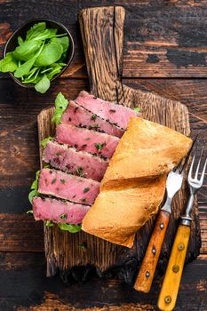 Grilled Ahi Tuna Steak and Avocado Sandwich with arugula on a cutting board. Dark wooden background. Top view.