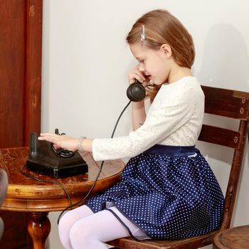 Cheerful little girl talking on a vintage telephone in the interior of the sixties of the last century.Retro style.