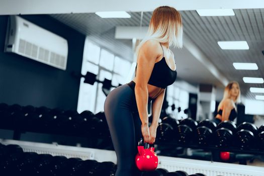 Curvy fit young blonde woman in sportswear lifting dumbbell in a gym