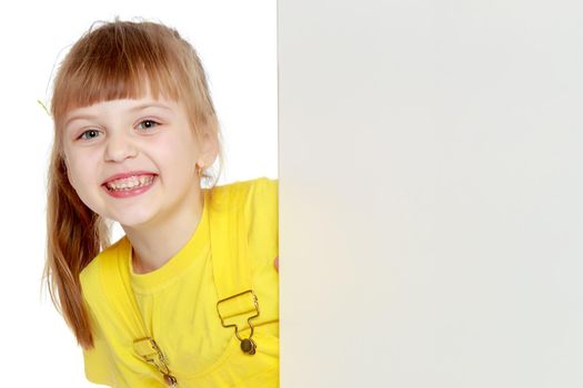 Girl with a short bangs on her head and bright yellow overalls.She crouched down on the white advertising banner.