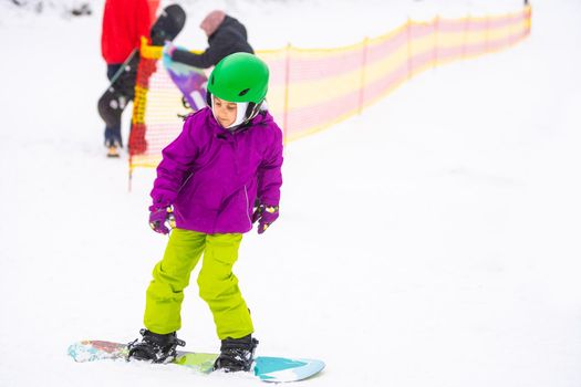 Snowboard Winter Sport. little girl learning to snowboard, wearing warm winter clothes. Winter background.