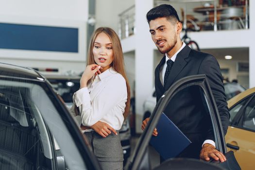 Man car dealer showing a woman buyer a new car in car salon