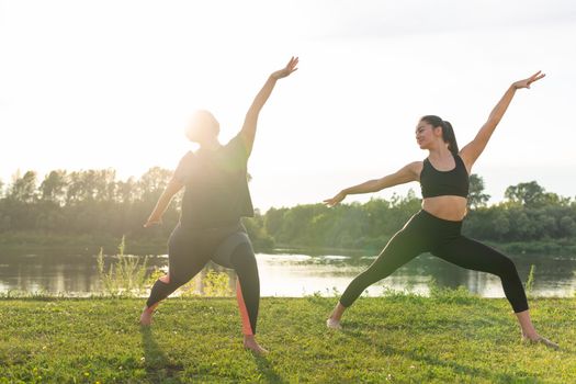 Harmony and healthy lifestyle concept - Young slim women in sportswear practicing yoga outdoors