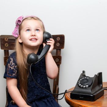 A sweet little girl is ringing on the old phone. The concept of a happy childhood, retro style, old things of the fifties of last century.