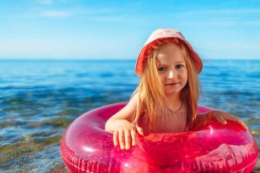 Happy little girl bathing in sea with pink circle and hat