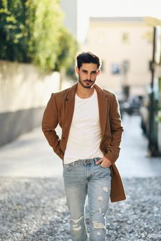 Young man wearing winter clothes in the street. Young bearded guy with modern hairstyle with coat, blue jeans and white t-shirt.