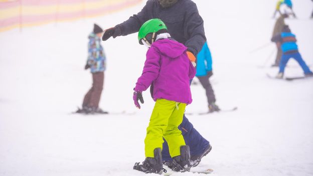 Instructors teach a child on a snow slope to snowboard