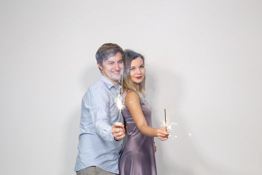 Party, celebration, event and holidays concept - man dressed in blue shirt and woman dressed in purple dress hold a firework stick.