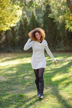 Beautiful young African American woman with afro hairstyle and green eyes wearing white winter dress walking in an urban park