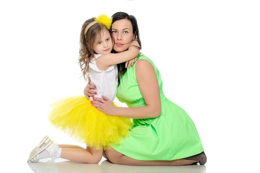 Beautiful young mother in a short green dress and her little beloved daughter in a yellow skirt.Daughter gently hugs the mother's neck.Isolated on white background.