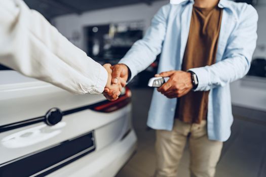 Car seller and buyer handshake at car dealership against a new car background