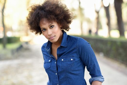 Young black woman with afro hairstyle standing in urban background. Mixed woman wearing blue shirt and shorts.