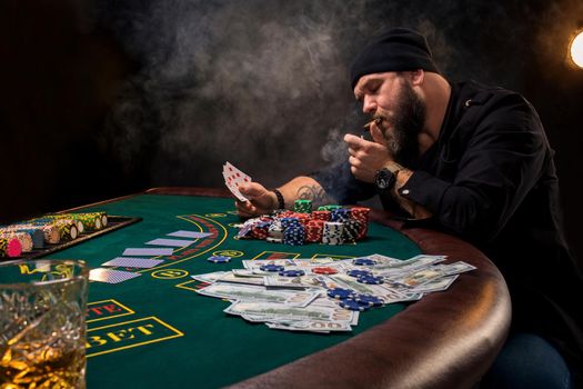 Man is playing poker with a cigar and a whiskey. A man winning all the chips on the table with thick cigarette smoke. The concept of victory