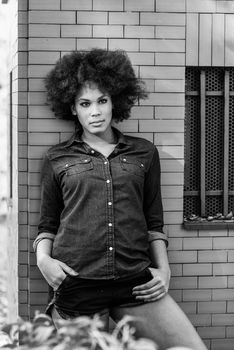 Young black woman with afro hairstyle standing in urban background. Mixed woman wearing blue shirt and shorts.
