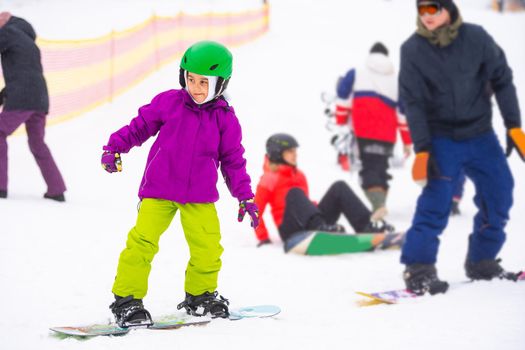 Little Cute Girl Snowboarding at ski resort in sunny winter day.