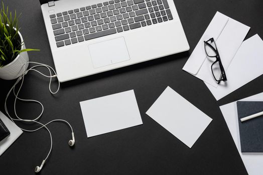 Top view of office workplace with digital gadgets. Flat lay black surface with laptop, green plant and white paper sheets. Top view coworking workspace with devices. Digital technology and mobility.