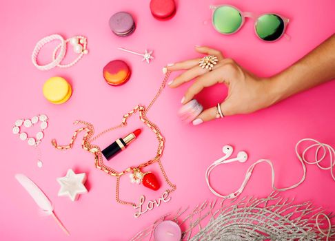 woman hands holding macaroons with lot of girl stuff on pink background, girls accessories concept close up