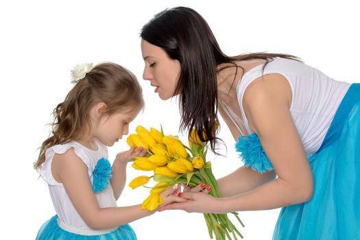 Beautiful young mother and little daughter in the same blue long skirts tutus , standing sideways to the camera ,admiring the bouquet of yellow tulips.Little girl enjoying the smell of flowers.Isolated on white background.