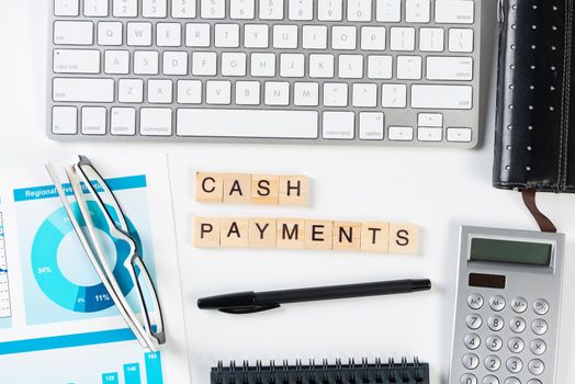 Cash payments concept with letters on wooden cubes. Still life of office workplace with supplies. Flat lay white surface with computer keyboard and notepad. Financial management and accounting.