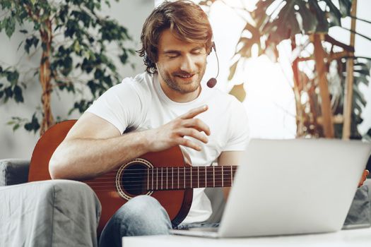 Young man watching guitar tutorial on his laptop at home