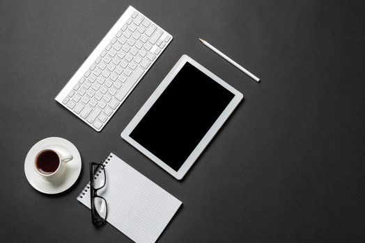 Top view of modern workplace with tablet computer. Flat lay black surface with keyboard, cup of coffee and notebook. Top view coworking workspace and freelance. Digital technology and home office.