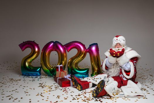 Stock photo of jolly Father Frost in festive clothing with long white beard outstretching his arms and smiling at camera under flying golden confetti. Isolated on grey background.