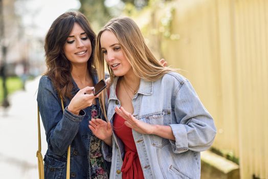 Two young women recording a voice message with smart phone outdoors. Girls using the voice recognition of the smartphone
