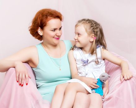 Mom and daughter are sitting on the couch. The concept of family happiness, parenthood, childhood. Isolated on white background.