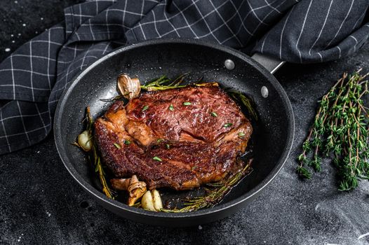 Roasted rib eye steak, ribeye beef meat in a pan. Black background. Top view.