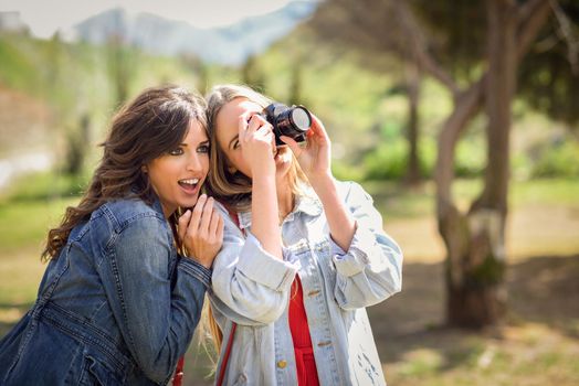 Two young tourist women taking photographs with analogic reflex camera in urban park. Travelers concept.