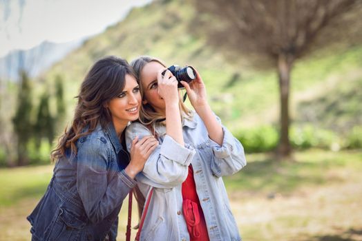 Two young tourist women taking photographs with analogic reflex camera in urban park. Travelers concept.