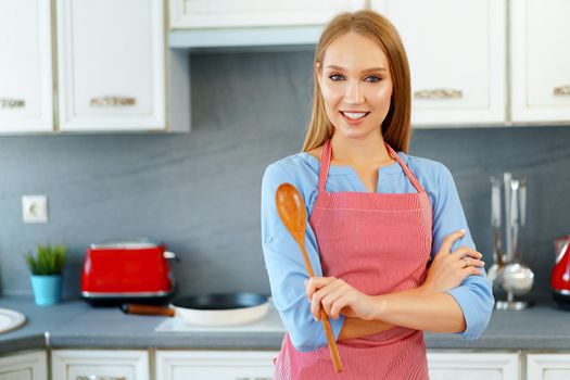 Attractive young woman in red apron standing in her kitchen, woman portrait