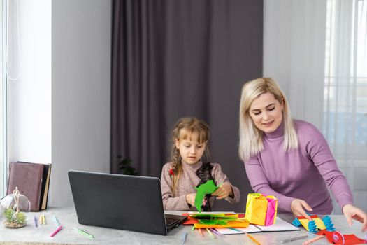 Child with mother have a fun cutting out scissors paper in preschool. mother and daughter make paper crafts