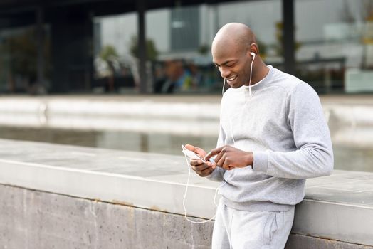 Attractive black man listening to music with headphones in urban background. Male in sportswear outdoors.