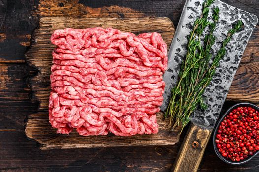 Raw mince beef, ground meat with herbs and spices on a wooden cutting board. Dark wooden background. Top view.
