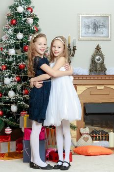 Adorable little twin girls hugging each other near the Christmas tree.