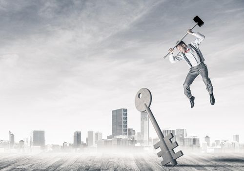 Determined businessman against cityscape breaking with hammer stone key figure